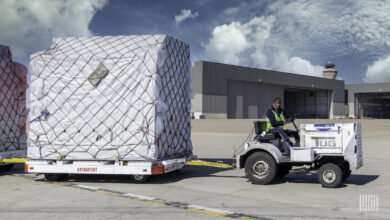 A small ground tug pulls a large pallet with wheels at an airport.