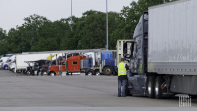 A man in a neon vest speaks to a semi truck driver through the driver side window.