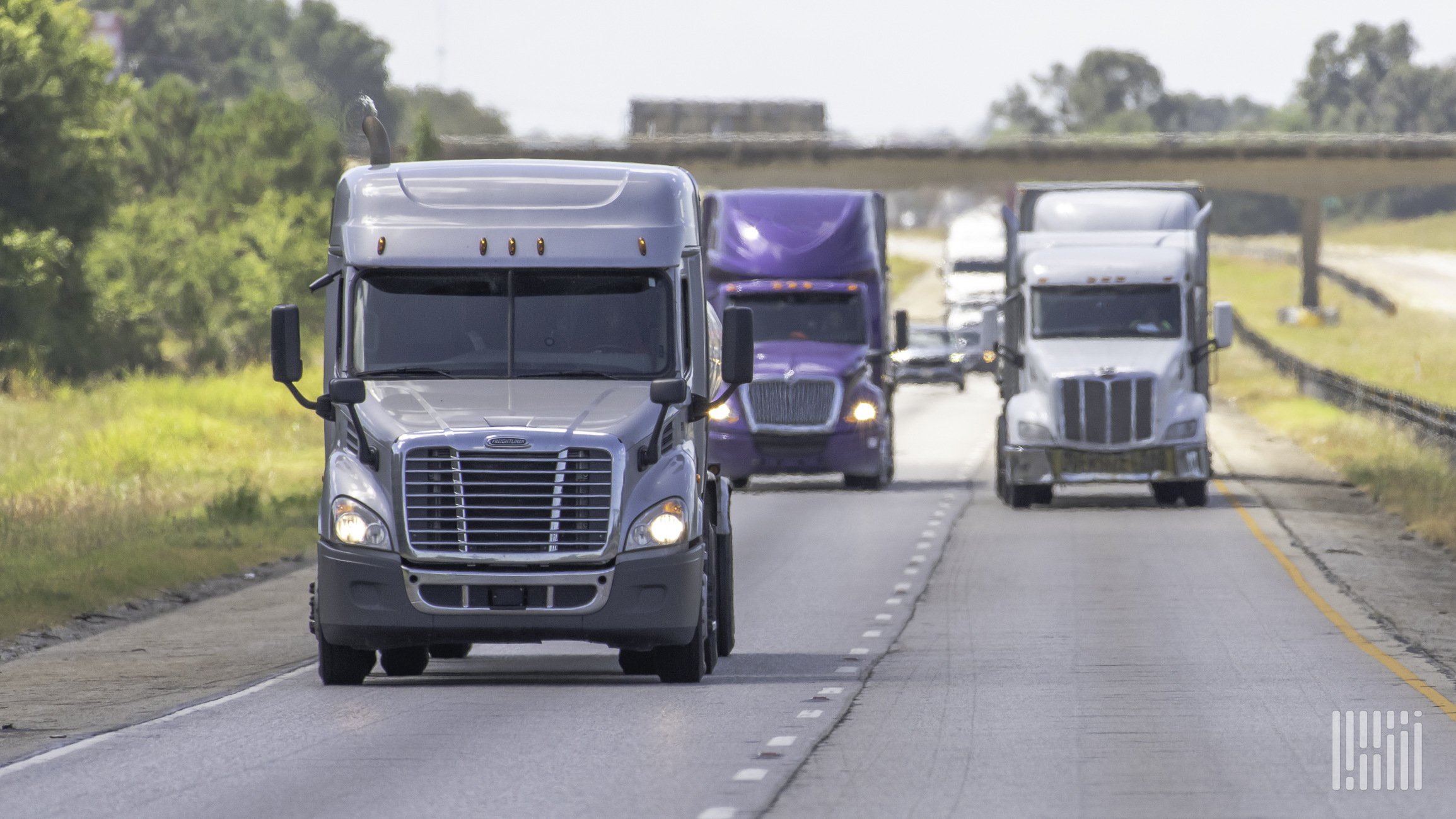 Three semi trucks travel down a major road.