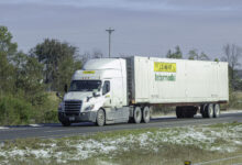 A white J.B. Hunt tractor pulling a J.B. Hunt intermodal container on a highway