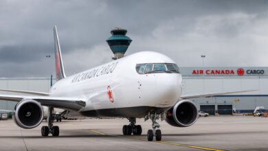 A black-white Air Canada Cargo jet in front of an Air Canada cargo terminal on a gray day.