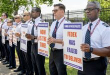 FedEx pilots in white, short-sleeve shirts stand side-by-side holding signs to protest FedEx's contract negotiations.